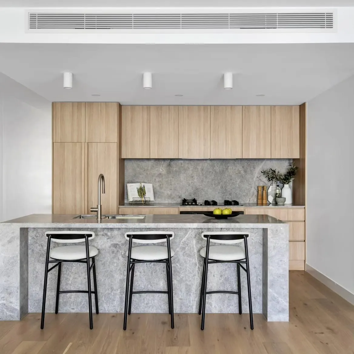 Timber kitchen with a grey stone island and black stools